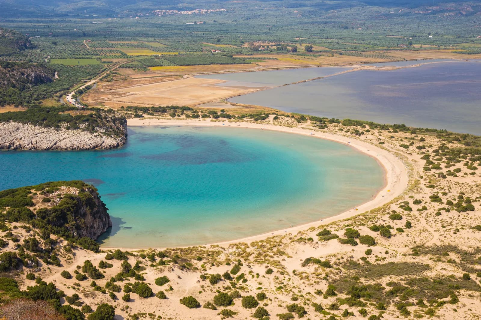 The omega-shaped bay of Voidokilia from above, turquoise water inside a curve of pale sand