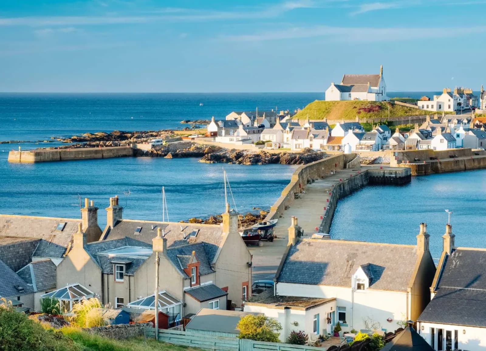 Findochty harbour on the Moray Firth — a curved stone breakwater and slate-roofed cottages above blue water